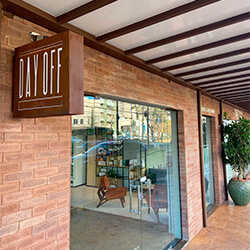 Unidade Ribeirão | DAY OFF CAFÉ - FIUSA Fachada em tijolos com placa de madeira da Unidade em Ribeirão do Day Off